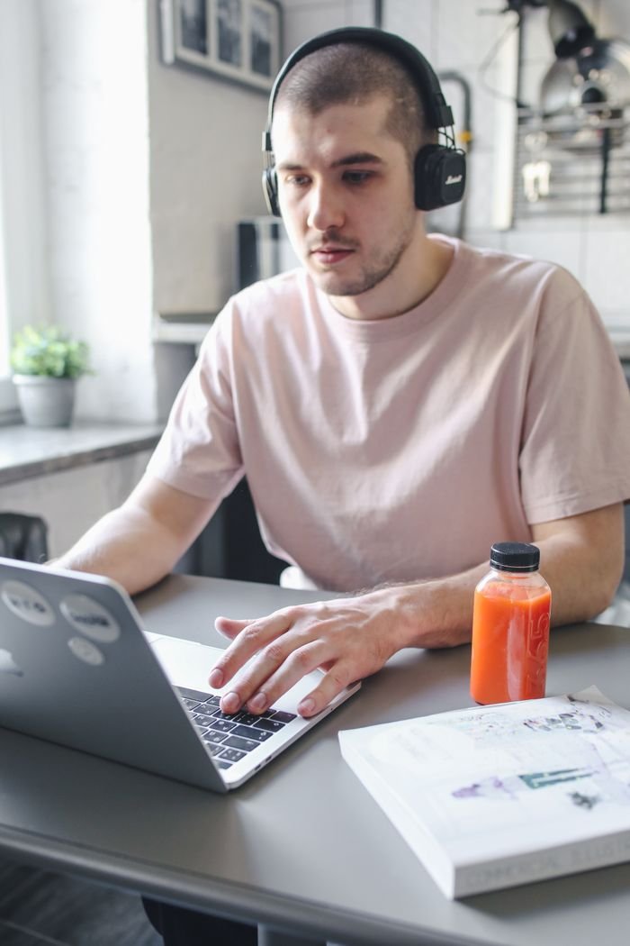 Young man working on laptop with headphones, focused on remote tasks indoors.